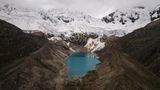 Ein blauer Gletschersee neben braunen Flächen, dahinter Eis