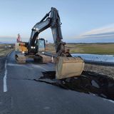 In Grindavik laufen Aufräumarbeiten. Ein Bagger ist an einem großen Loch an einer Straße am Werk.