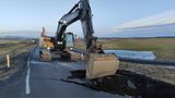 In Grindavik laufen Aufräumarbeiten. Ein Bagger ist an einem großen Loch an einer Straße am Werk.