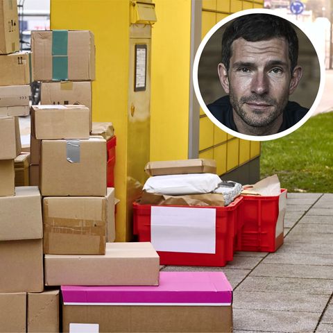 Ein Stapel Pakete lagert neben einem DHL-Auto auf dem Bürgersteig