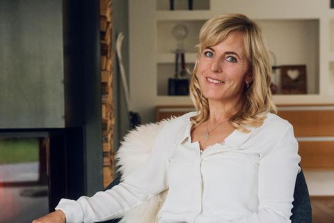 Martina Ertl sitzt auf einem Stuhl und lächelt in die Kamera