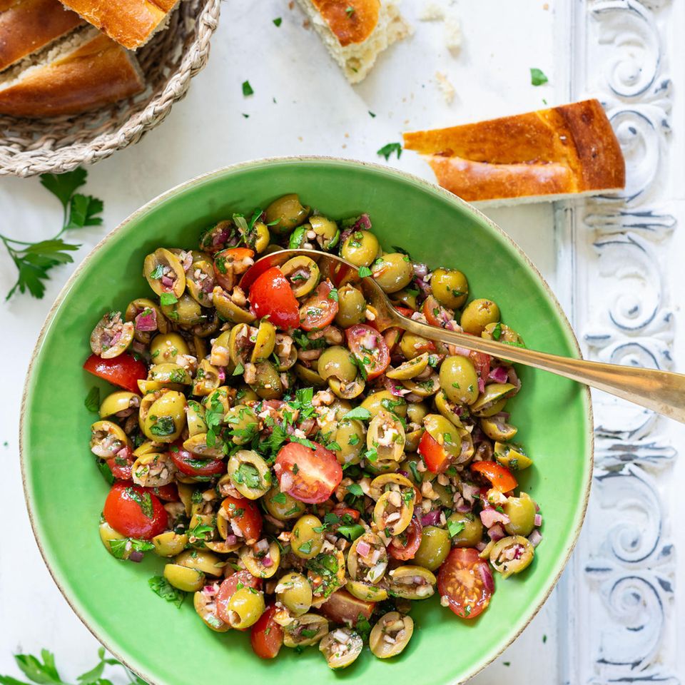 Bazrkani   Armenischer Olivensalat  Für 4 Portionen  Zutaten:  200 g entsteinte grüne Oliven 1 rote Zwiebel  5–10 Cherrytomaten  2 EL Tomatenmark  1 EL Granatapfelsirup/Granatapfelkonzentrat (alternativ Balsamico-Essig oder Balsamico-Creme)  2 EL Olivenöl  1⁄2 TL schwarzer Pfeffer aus der Mühle  1⁄2 TL edelsüßes Paprikapul- ver  1 Prise Kreuzkümmel 1⁄2 TL getr. Thymian  1⁄2 Bund Petersilie 50 g Walnusskerne Salz nach Bedarf     Zubereitung:  1. Oliven längs halbieren oder vierteln. Zwiebel schälen und fein würfeln. Tomaten waschen, trocken tupfen und vierteln. Alles in einer Schüssel miteinander vermengen.  2. Für das Dressing Tomatenmark, Granatapfelsirup und Olivenöl miteinander vermischen, bei Bedarf 1 TL Wasser hinzufügen und glattrühren. Mit Pfeffer, Paprikapulver, Kreuzkümmel und Thymian abschmecken. Dressing zum Salat geben und alles gut vermengen. Einige Minuten ziehen lassen.  3. Währenddessen Petersilie waschen, trocken schütteln und fein hacken. Walnusskerne ebenfalls hacken. Petersilie und Walnusskerne zum Salat geben und vermengen.  4. Probieren und bei Bedarf salzen (meist reicht jedoch der Salzgehalt der Oliven aus). Sofort servieren oder im Kühlschrank eine halbe Stunde ziehen lassen.     »Bazrkani« stammt aus den Dörfern der Region Musa Ler (heutige Türkei), wo im ehemaligen Osmanischen Reich überwiegend armenische Menschen lebten und den fruchtbaren Boden und das günstige Klima für die Landwirtschaft nutzten. Der Oliven- salat Bazrkani wird auch »Hirtensalat aus Musa Ler« genannt. Die Schafhirten konnten ihn mit nur wenigen Zutaten auch draußen bei ihrer Herde zubereiten. Anfang des 20. Jahrhunderts brachten armenische Überlebende des Genozids dieses Gericht schließlich in ihre neue Heimat, die Republik Armenien.