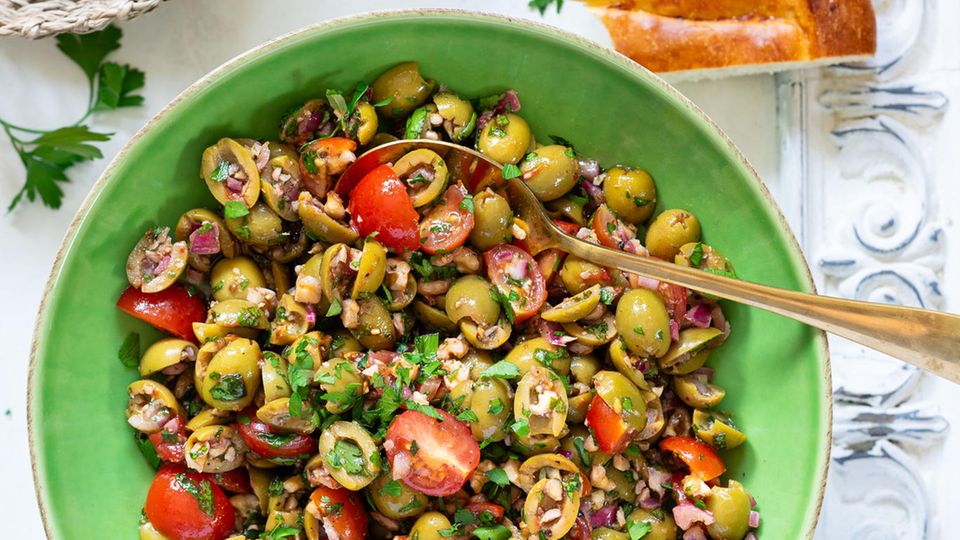 Bazrkani   Armenischer Olivensalat  Für 4 Portionen  Zutaten:  200 g entsteinte grüne Oliven 1 rote Zwiebel  5–10 Cherrytomaten  2 EL Tomatenmark  1 EL Granatapfelsirup/Granatapfelkonzentrat (alternativ Balsamico-Essig oder Balsamico-Creme)  2 EL Olivenöl  1⁄2 TL schwarzer Pfeffer aus der Mühle  1⁄2 TL edelsüßes Paprikapul- ver  1 Prise Kreuzkümmel 1⁄2 TL getr. Thymian  1⁄2 Bund Petersilie 50 g Walnusskerne Salz nach Bedarf     Zubereitung:  1. Oliven längs halbieren oder vierteln. Zwiebel schälen und fein würfeln. Tomaten waschen, trocken tupfen und vierteln. Alles in einer Schüssel miteinander vermengen.  2. Für das Dressing Tomatenmark, Granatapfelsirup und Olivenöl miteinander vermischen, bei Bedarf 1 TL Wasser hinzufügen und glattrühren. Mit Pfeffer, Paprikapulver, Kreuzkümmel und Thymian abschmecken. Dressing zum Salat geben und alles gut vermengen. Einige Minuten ziehen lassen.  3. Währenddessen Petersilie waschen, trocken schütteln und fein hacken. Walnusskerne ebenfalls hacken. Petersilie und Walnusskerne zum Salat geben und vermengen.  4. Probieren und bei Bedarf salzen (meist reicht jedoch der Salzgehalt der Oliven aus). Sofort servieren oder im Kühlschrank eine halbe Stunde ziehen lassen.     »Bazrkani« stammt aus den Dörfern der Region Musa Ler (heutige Türkei), wo im ehemaligen Osmanischen Reich überwiegend armenische Menschen lebten und den fruchtbaren Boden und das günstige Klima für die Landwirtschaft nutzten. Der Oliven- salat Bazrkani wird auch »Hirtensalat aus Musa Ler« genannt. Die Schafhirten konnten ihn mit nur wenigen Zutaten auch draußen bei ihrer Herde zubereiten. Anfang des 20. Jahrhunderts brachten armenische Überlebende des Genozids dieses Gericht schließlich in ihre neue Heimat, die Republik Armenien.