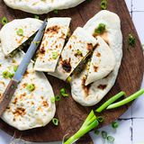 Jingalov Hats  Mit Kräutern gefüllte Brotfladen  4 Portionen     Zutaten:  Für den Teig:  150 ml lauwarmes Wasser 1 TL grobes Salz  200 g Weizenmehl (Type 550) + etwas Mehl für die Arbeitsfläche  etwas Pflanzenöl  Für die Füllung:  450 g unterschiedliche Kräuter und grünes Blattgemüse nach Geschmack (ideal ist eine geschmacklich ausgewogene Mischung aus nicht zu harten Sorten wie etwa Koriander, Dill, Petersilie, Estragon, Spinat, Mangold, Rucola, Kohlrabiblätter, Karottengrün, Kerbel, Basilikum, Borretsch, Bärlauch, Löwenzahn, Radieschen- grün, Brunnenkresse, Blattkohl, Portulak und andere bekömmliche Krautpflanzen)  2 Frühlingszwiebeln  2 TL edelsüßes Paprikapulver 1 TL Salz  1⁄2 TL Cayennepfeffer  2 TL Zitronensaft  1 EL Pflanzenöl     Zubereitung:  1. Für den Teig in einer großen Rührschüssel 150 ml lauwarmes Wasser mit Salz mischen. Portionsweise das Mehl einrühren und kurz zu einem klebrigen Teig kneten. Arbeitsfläche mit Mehl bestäuben und den Teig darauf mit den Händen einige Minuten lang kneten, bis er sich glatt und nicht mehr so klebrig anfühlt.  2. Rührschüssel säubern und innen dünn mit etwas Öl bestreichen. Den Teig zu einem großen Kloß formen, in die Schüssel geben und mit einem Küchenhandtuch abgedeckt mindestens 20 Minuten bis zu 1 Stunde ruhen lassen.  3. Währenddessen für die Füllung alle Kräuter und Blattgemüse waschen, trocken schütteln und fein hacken. Die Frühlingszwiebel putzen, waschen und in sehr feine Ringe schneiden. In einer Schüssel Kräuter und Frühlingszwiebeln mit Paprikapulver, Salz, Cayennepfeffer, Zitronensaft und Öl mischen und mit den Händen leicht durchkneten.  4. Anschließend die Arbeitsfläche erneut mit Mehl bestäuben. Den Teig darauf legen und in vier gleich große Teile teilen und jeden Teil zu einer Kugel formen.  5. Auf der bemehlten Arbeitsfläche die erste Kugel mithilfe eines Nudelholzes dünn kreisförmig ausrollen, der Teig sollte zum Schluss etwa die Größe eines Desserttellers haben. Etwa 100 g der Kräuterfüllung in die Mitte des Teiges geben – keine Sorge, das sieht zwar nach einer viel zu großen Menge aus, aber sie ist genau richtig.  6. Den Teig vorsichtig am rechten und linken Rand anheben und mit den Fingern mittig über der Füllung zusammen- drücken. Von dieser Mitte aus jeweils nach oben und nach unten genauso verfahren und den restlichen offenen Rand zusammendrücken, sodass eine durchgehende Naht entsteht. Die beiden Spitzen gut zusammenpressen und etwas einklappen, damit nichts herausfallen kann. Jetzt müsste es wie eine riesige Teigtasche aussehen. Mit der Handkante die Teignaht andrücken, damit der Fladen gut verschlossen ist und sich die Naht beim Garen nicht öffnet. Den Fladen nun mit der Naht nach unten auf die Arbeitsfläche legen und mit der Handfläche leicht flachdrücken, bis er nur noch etwa 1 cm dick ist.  7. Mit der zweiten Teigkugel ebenso verfahren, die dritte und vierte Kugel noch ruhen lassen.  8. Eine ausreichend große Pfanne auf dem Herd erhitzen (ideal sind gusseiserne oder schmiedeeiserne Pfannen, aber auch Pfannen mit einer hohen Wärmeleitfähigkeit funktionieren hierfür gut). Einen Fladen mit der Naht nach unten hinein- legen und bei mittlerer Hitze etwa 3 Minuten garen, danach wenden und weitere 2 Minuten garen. Beide Seiten sollten goldbraun sein und nicht mehr roh aussehen. Bei Bedarf die Seiten jeweils noch 1–2 Minuten garen. Herausnehmen und auf eine Servierplatte geben. Den zweiten gefüllten Fladen ebenso garen.  9. Während die ersten zwei Fladen in der Pfanne garen, auch die beiden verbliebenen Teigfladen mit der Kräutermischung füllen, verschließen, plattdrücken und nacheinander in der Pfanne garen.  10. Jingalov Hats sofort warm servieren, sie schmecken aber kalt ebenso gut. Im Kühlschrank halten sich die gefüllten Fladen etwa 3 Tage, im Eisfach bis zu 2 Monate. Tiefgekühlte Fladen im Ofen bei 200 °C Umluft etwa 10 Minuten knusprig auf- backen.     »Jingalov Hats« bedeutet wörtlich übersetzt »Brot mit Kräutern«, wobei »Jingal« ein Dialektwort ist und vom persischen »jangal« abstammt, was »Laubwald« bedeutet. Diese mit frischen Kräutern gefüllten flachen Brotfladen sind eine Spezialität der Regionen Arzach (Bergkarabach) und Syunik, die besonders fruchtbar und zugleich bergig sind. Nach traditionellem Rezept werden mindestens zehn verschiedene Kräuter- und Blattgemüsesorten dafür verarbeitet. Armenische Familien bereiten die Fladen meist direkt auf der Stahlplatte ihres Holzofens oder einer Grillplatte zu.  Jingalov Hats können Sie als Frühstück, Mittag- oder Abendessen oder als Snack zwischendurch genießen.