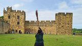 Alnwick Castle, eine Burg, in deren Hof jemand einen Besen hält. Hier findet das Flugtraining im "Harry Potter"-Film statt