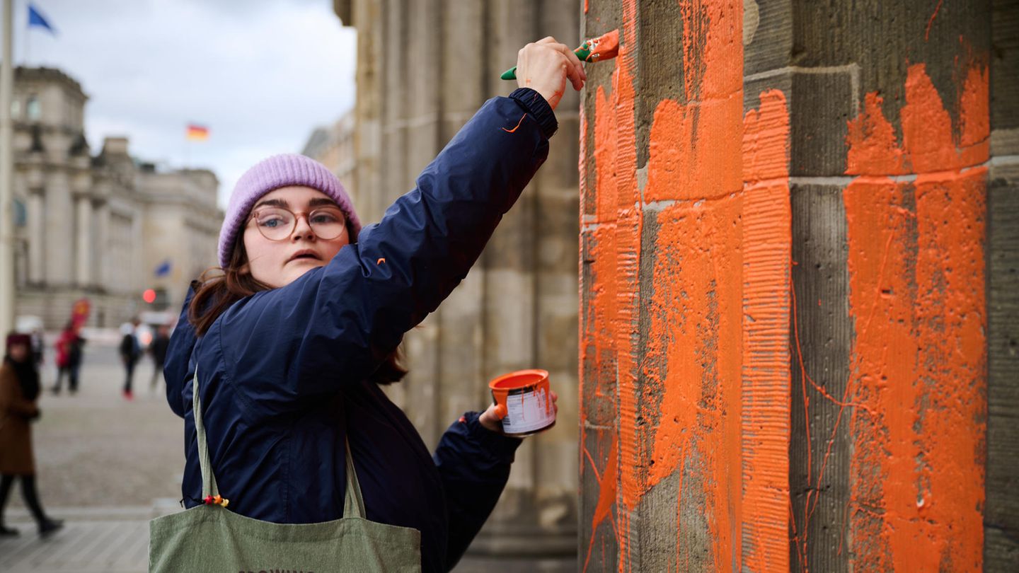 Eine Klimaaktivistin bemalt das Brandenburger Tor mit oranger Farbe