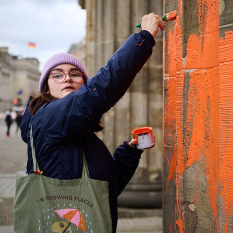 Eine Klimaaktivistin bemalt das Brandenburger Tor mit oranger Farbe