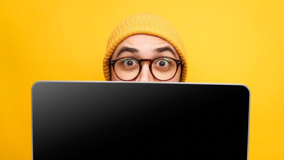 Black Week 2023 Apple Deals: Hipster mit gelber Strickmütze guckt über Laptoprand