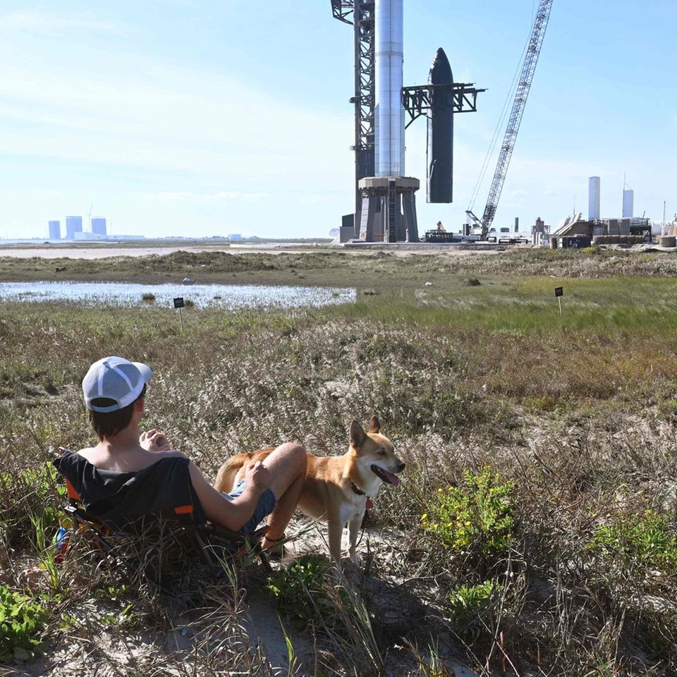 Boca Chica, Texas, USA. Wahrlich einen Platz in der ersten Reihe hat dieser Mann ergattert. Im Hintergrund laufen die Startvorbereitungen für "Starship". Der zweite Test des größten jemals gebauten Raketensystems der Raumfahrtgeschichte ist allerdings von Freitag auf Samstag verschoben worden. Es müsse noch eine Antriebseinheit an einer Steuerfläche ausgetauscht werden, schrieb Elon Musk am Donnerstag beim ihm gehörenden Kurznachrichtendienst X, früher Twitter. "Deswegen ist der Start auf Samstag verschoben." Um 14.00 Uhr MEZ solle sich am Samstag ein 20-minütiges Startfenster für das "Starship" öffnen, teilte SpaceX kurz darauf mit.  Wenn Mann und Hund also viel Geduld haben, erleben sie den Start unmittelbar mit. Allerdings war "Starship" Mitte April erstmals zu einem unbemannten Teststart aufgebrochen – und vier Minuten später taumelnd explodiert und zerbrochen. Es wäre das größere Spektakel – aber gegen herabstürzende Trümmer würde das Cap nicht helfen.     