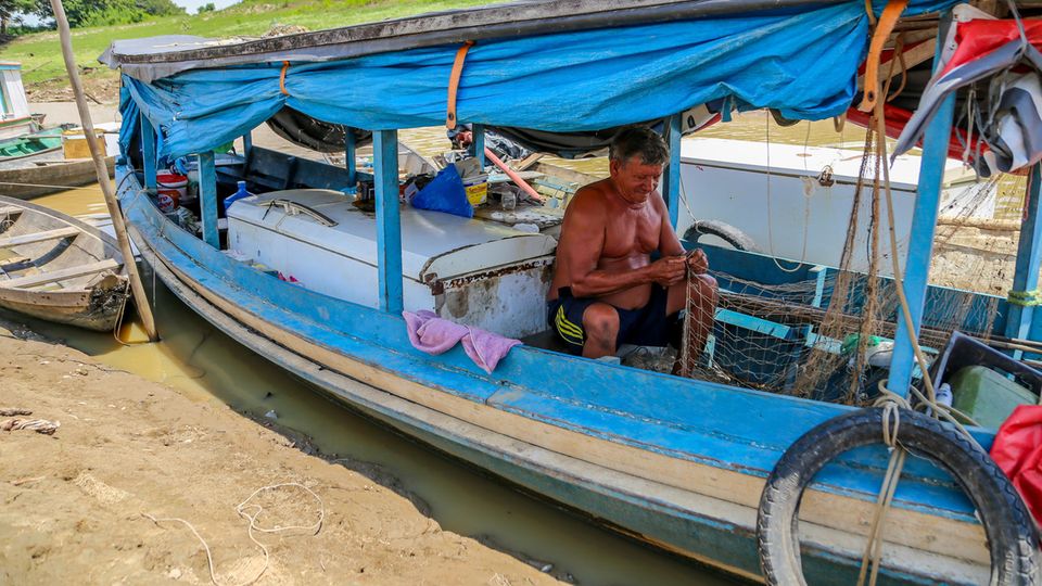 Fast auf dem Trockenen: Ein Fischer sitzt neben einem Kühlschrank in seinem Boot und flickt ein Netz. Rausfahren und fischen ist unmöglich, dafür sind die Gewässer nicht mehr tief genug. Die Pegelstände einiger der wichtigsten Flüsse waren zuletzt in noch nie da gewesenem Maße gesunken.