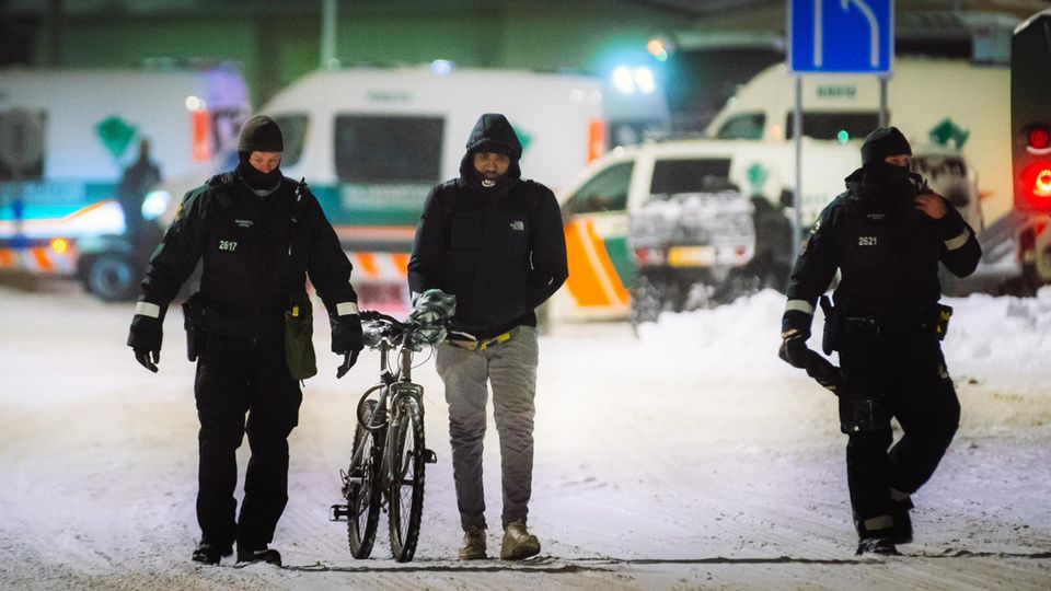 Ein Migrant (M) geht mit einem Fahrrad zwischen Beamten an der Grenzstation Vartius