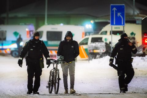 Ein Migrant (M) geht mit einem Fahrrad zwischen Beamten an der Grenzstation Vartius