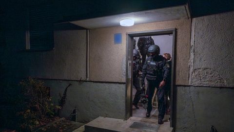 Polizisten verlassen während einer Wohnungsdurchsuchung ein Haus in München
