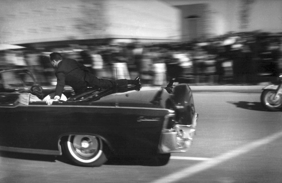 Die Dynastie: Sekunden nach dem tödlichen Schuss auf John F. Kennedy, rast die Limousine Richtung Krankenhaus. First Lady Jacqueline "Jackie" Kennedy beugt sich auf der Rückbank über den verwundeten Präsidenten. Agent Clinton Hill beschützt ihn hektisch am Heck des Fahrzeugs. Sekunden nach dem tödlichen Schuss auf John F. Kennedy, rast die Limousine Richtung Krankenhaus. First Lady Jacqueline "Jackie" Kennedy beugt sich auf der Rückbank über den verwundeten Präsidenten. Agent Clinton Hill beschützt ihn hektisch am Heck des Fahrzeugs.
