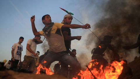Ein jugendlicher Palästinenser wirft Steine, während vor ihm Flammen lodern