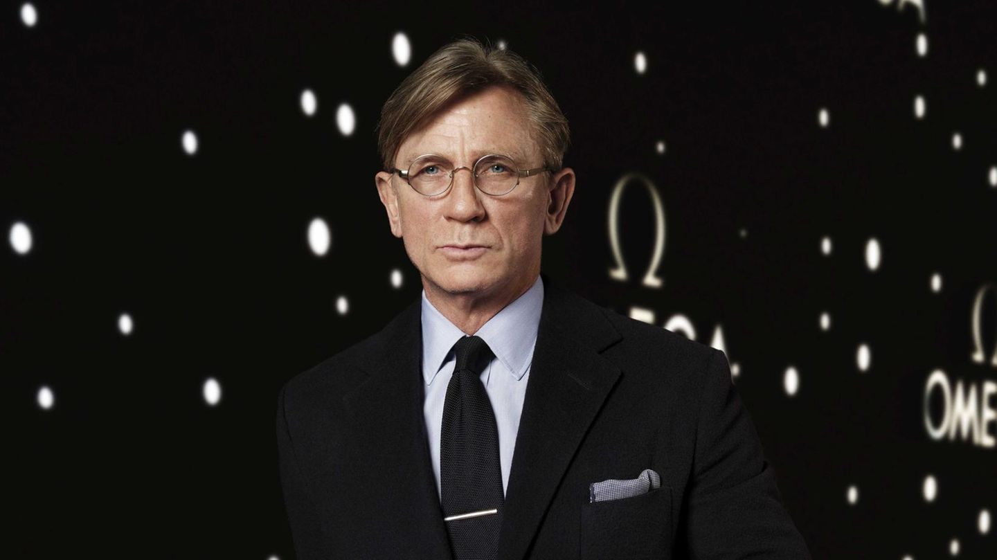 Schauspieler Daniel Craig im Anzug und mit Nickelbrille vor dunklem Hintergrund
