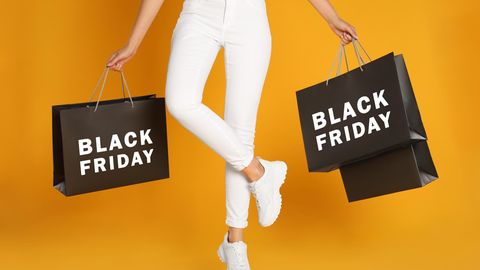 Black Friday: Eine Frau steht mit Black-Friday-Einkaufstüten in der Hand und ist glücklich