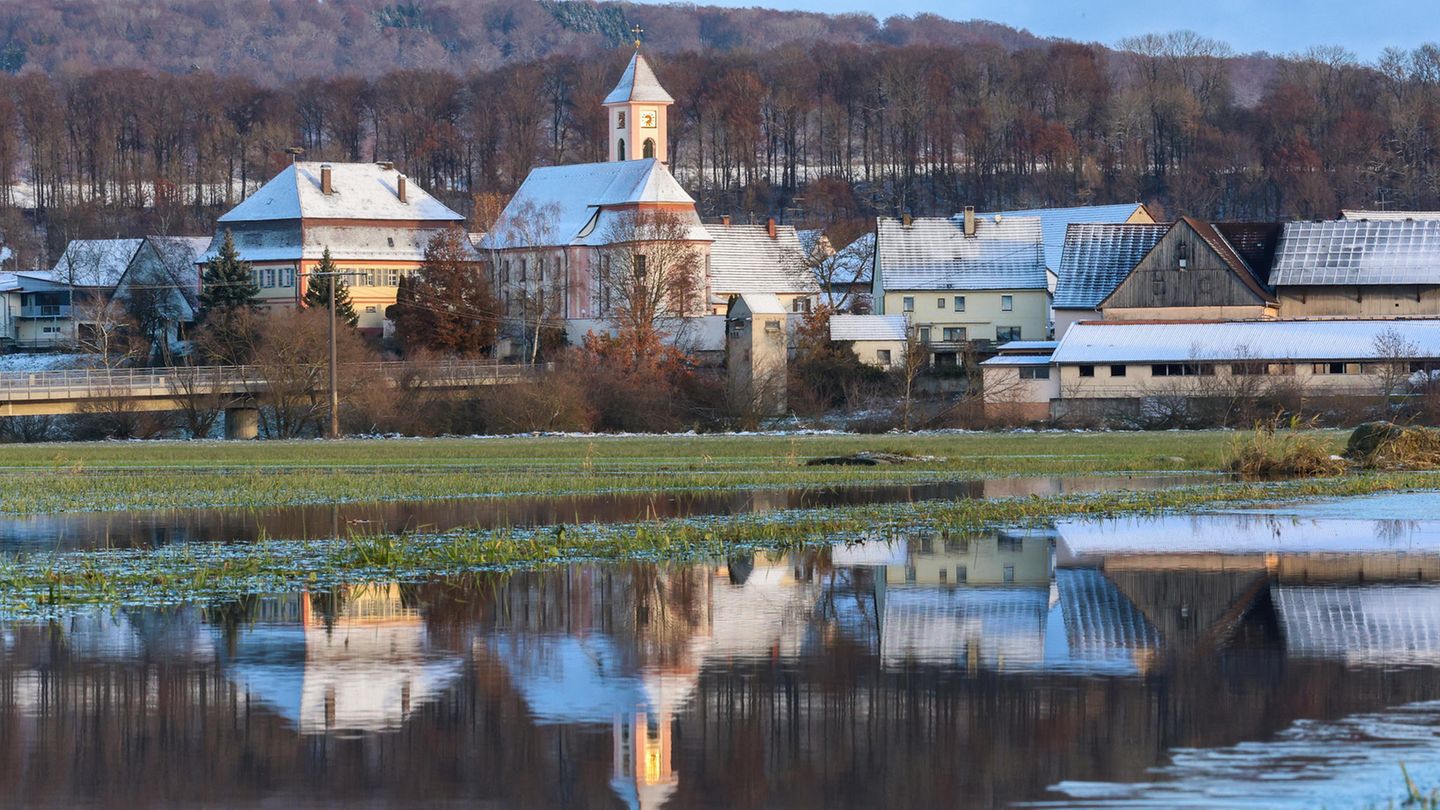 In Riedlingen (Baden-Württemberg) spiegeln sich schneebedeckte Dächer in einer überfluteten Wiese