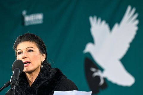Sahra Wagenknecht spricht auf einer Bühne in ein Mikrofon. Im Hintergrund eine Friedenstaube
