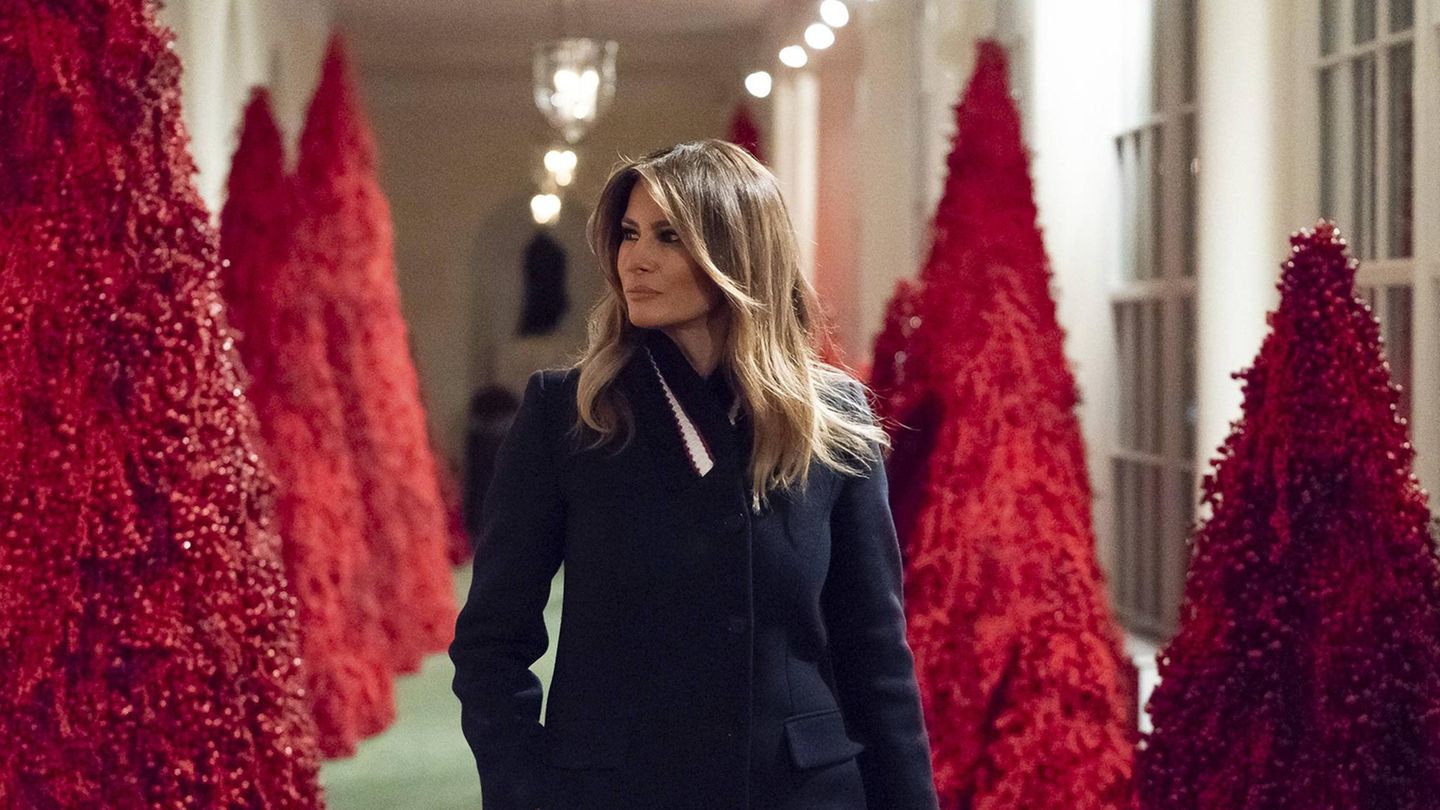 Melania Trump läuft an einer Allee mit roten Weihnachtsbäumen vorbei im Weißen Haus