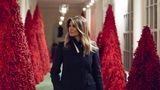 Melania Trump läuft an einer Allee mit roten Weihnachtsbäumen vorbei im Weißen Haus