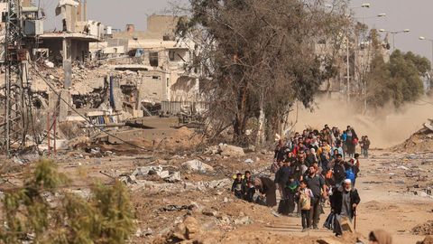 Ein Menschenstrom geht eine zerstörte Straße entlang