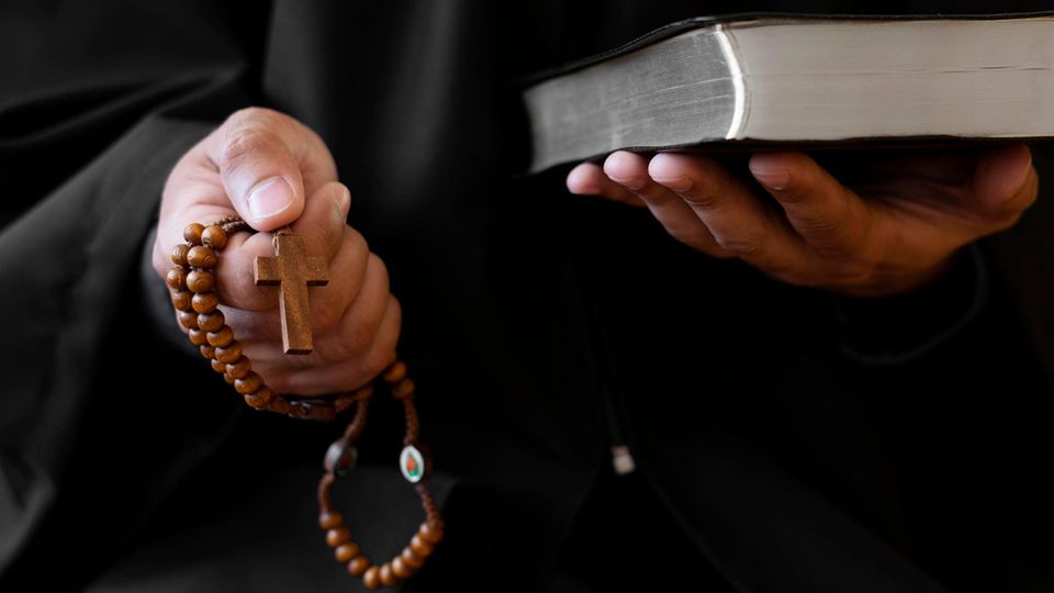 Exorzismus: Ein Priester hält ein Kreuz und eine Bibel in der Hand
