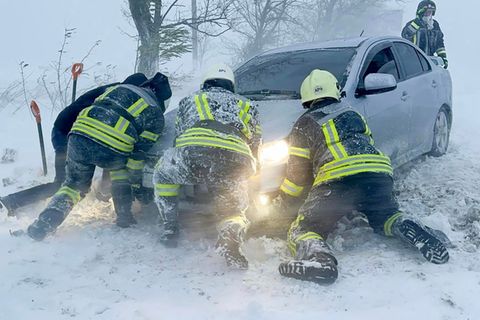 Ukrainische Rettungskräfte versuchen, ein im Schnee steckengebliebenes Auto auf der Autobahn in der Region Odessa zu schieben