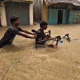 Ein Mann schiebt einen anderen Mann im Rollstuhl durch Hochwasser