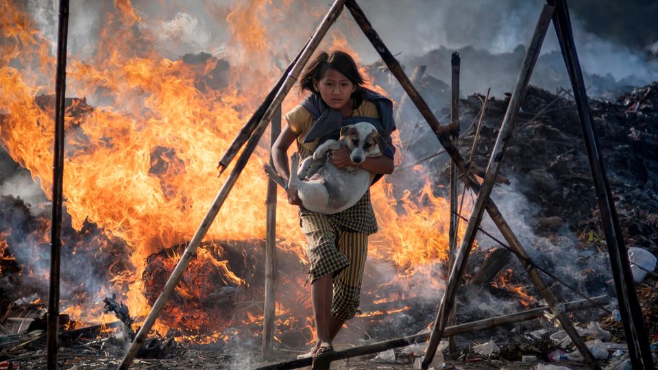 Ein junges Mädchen rennt mit einem Hund auf dem Arm durch lodernde Flammen