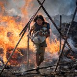 Ein junges Mädchen rennt mit einem Hund auf dem Arm durch lodernde Flammen
