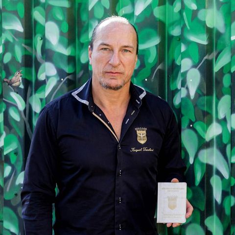 Peter Fitzek steht mit einem Ausweis in der linken Hand neben einem Schild "Königreich Deutschland"