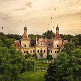 Über einem alten Schloss fliegen Vögel im Morgenlicht
