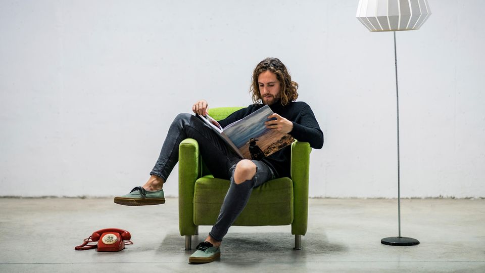 Junger Mann sitzt in einem Sessel und liest ein Buch