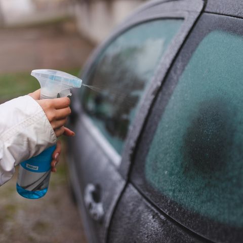 Nahaufnahme einer Frau, die ein Abtauspray auf ihr Autofenster anwendet