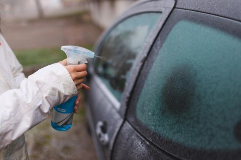 Nahaufnahme einer Frau, die ein Abtauspray auf ihr Autofenster anwendet