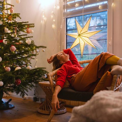 Advent: Ein weihnachtlich geschmücktes Zimmer mit Tannenbaum und einer Frau, die auf einem Sessel relaxt