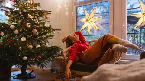 Advent: Ein weihnachtlich geschmücktes Zimmer mit Tannenbaum und einer Frau, die auf einem Sessel relaxt