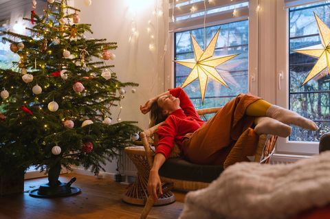 Advent: Ein weihnachtlich geschmücktes Zimmer mit Tannenbaum und einer Frau, die auf einem Sessel relaxt