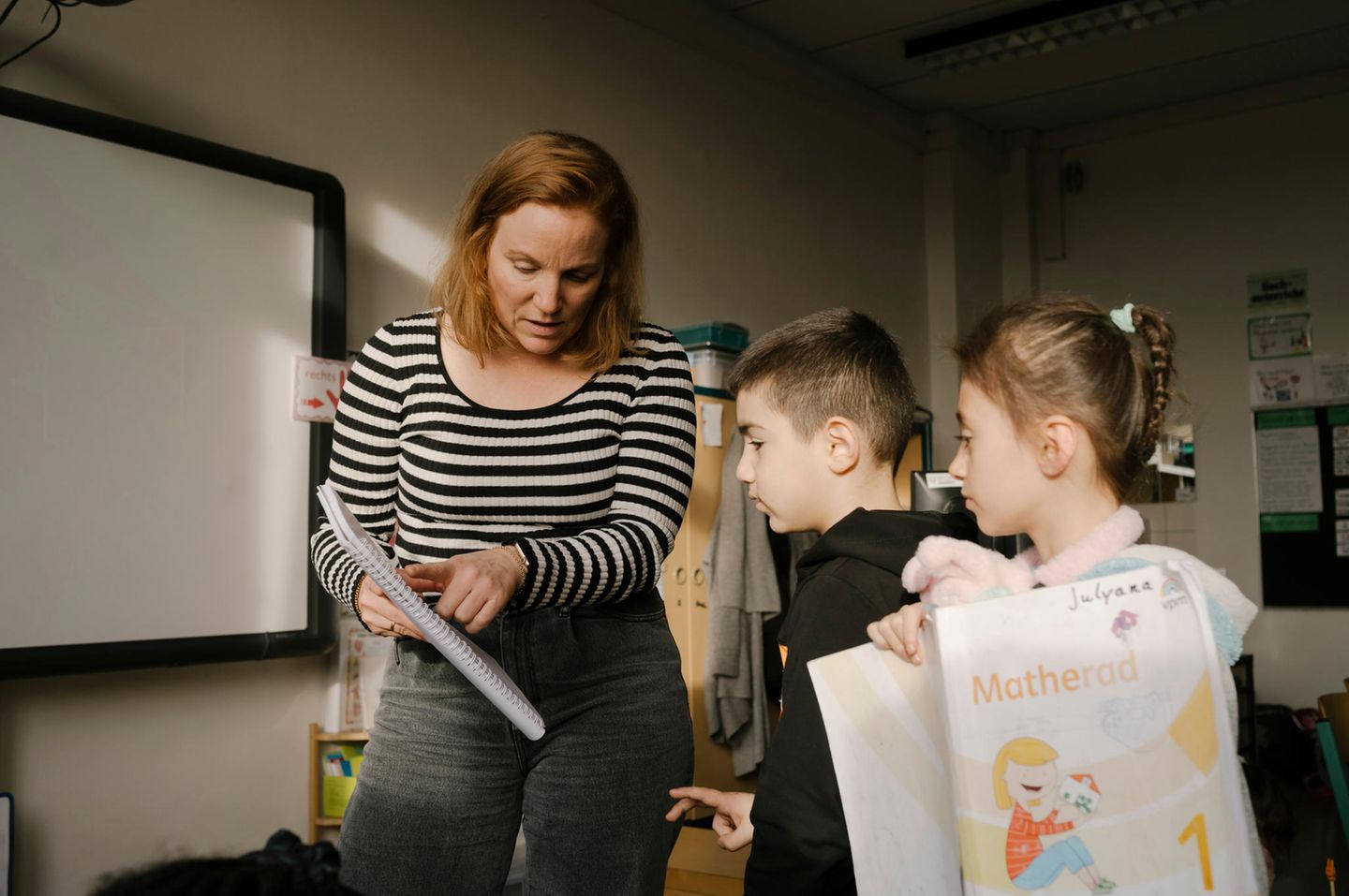 Eine Lehrerin erklärt zwei Kindern eine Aufgabe in der Klasse