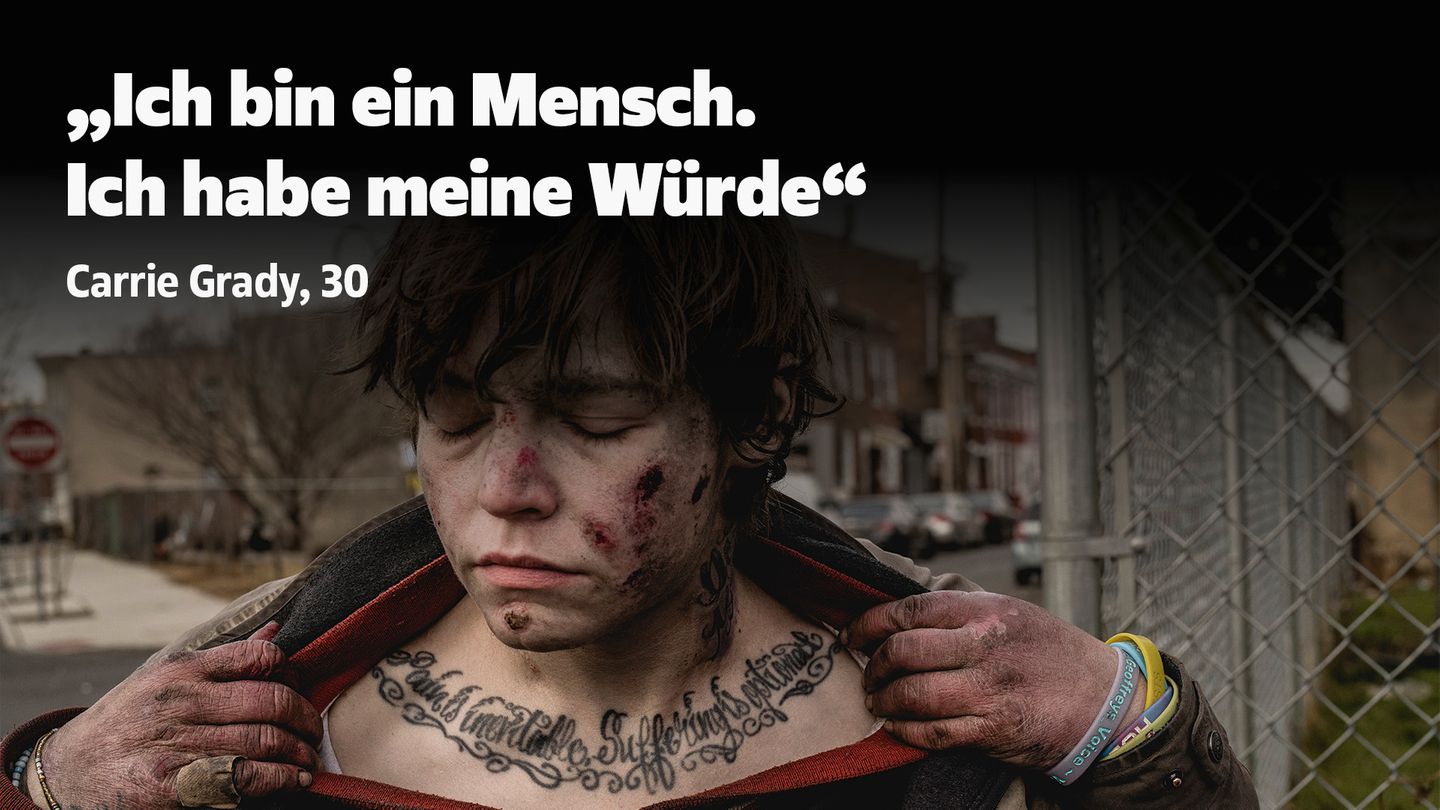 Eine junge Frau mit Wunden im Gesicht zieht ihre Kleidung zur Seite um ein Tattoo zu zeigen ihre Augen sind geschlossen