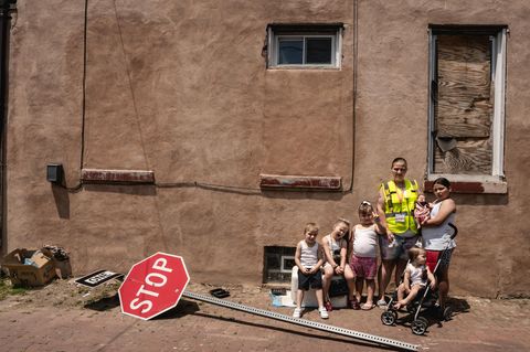 Eine Frau steht mit 5 kleinen Kindern vor einer Hauswand vor ihr liegt ein Stoppschild auf der Erde