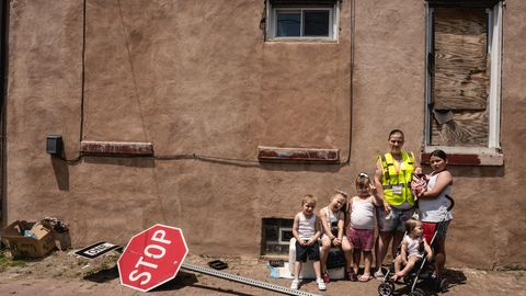 Eine Frau steht mit 5 kleinen Kindern vor einer Hauswand vor ihr liegt ein Stoppschild auf der Erde