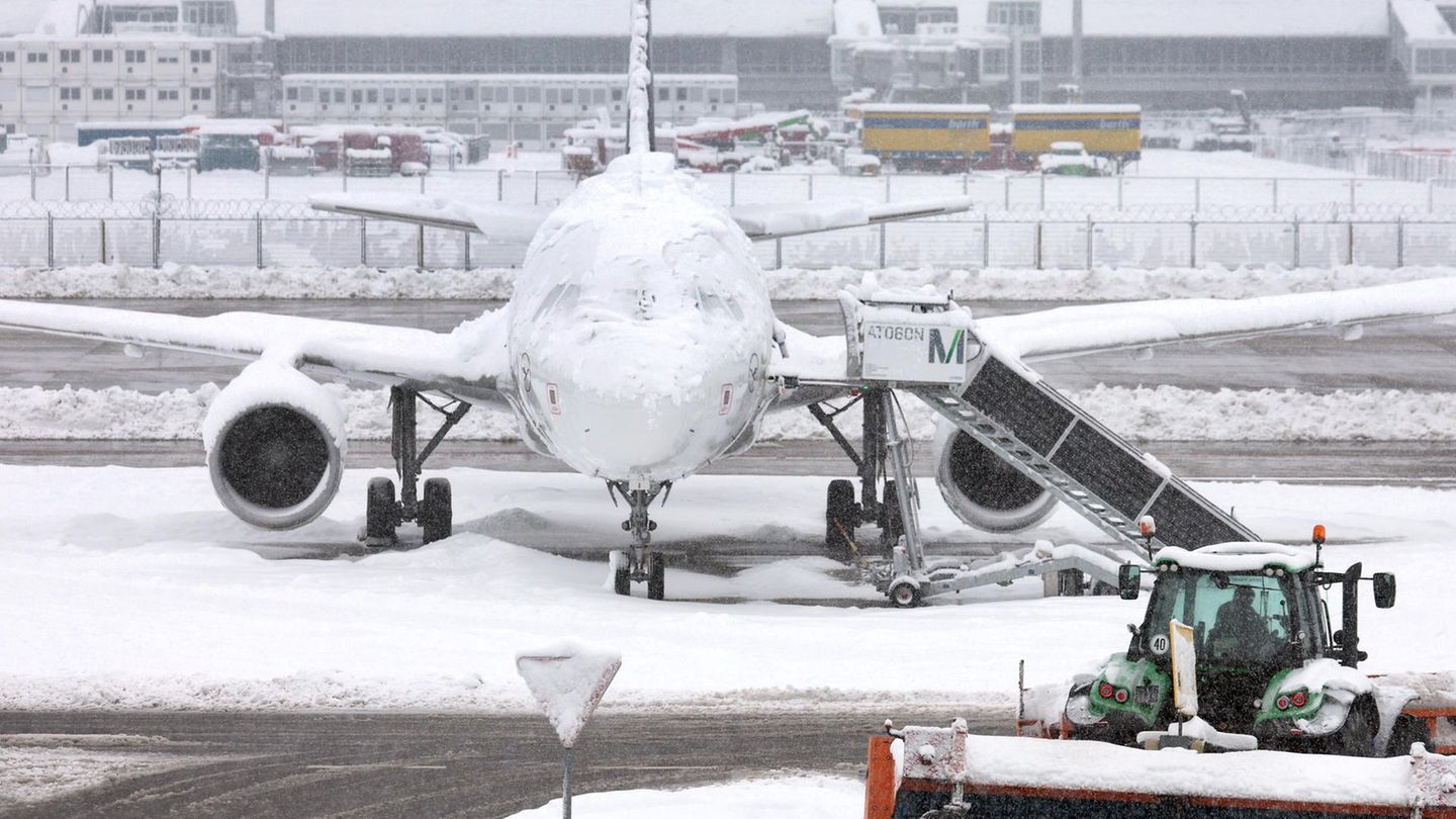 Ein Schneeräumer fährt im Schneetreiben auf dem Münchner Flughafen vor einer Maschine entlang