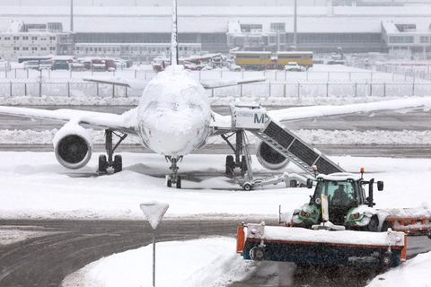 Ein Schneeräumer fährt im Schneetreiben auf dem Münchner Flughafen vor einer Maschine entlang