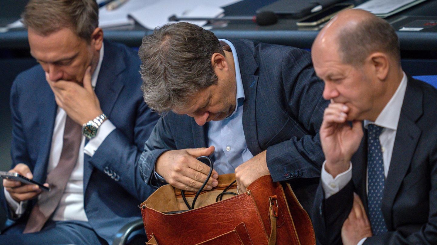 Robert Habeck kramt in seiner Tasche zwischen Christian Lindner und Olaf Scholz