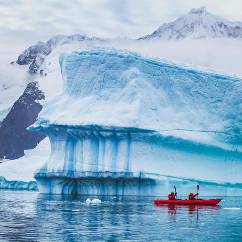Menschen paddeln mit einem Kajak in der Nähe eines Eisbergs in der Antarktis