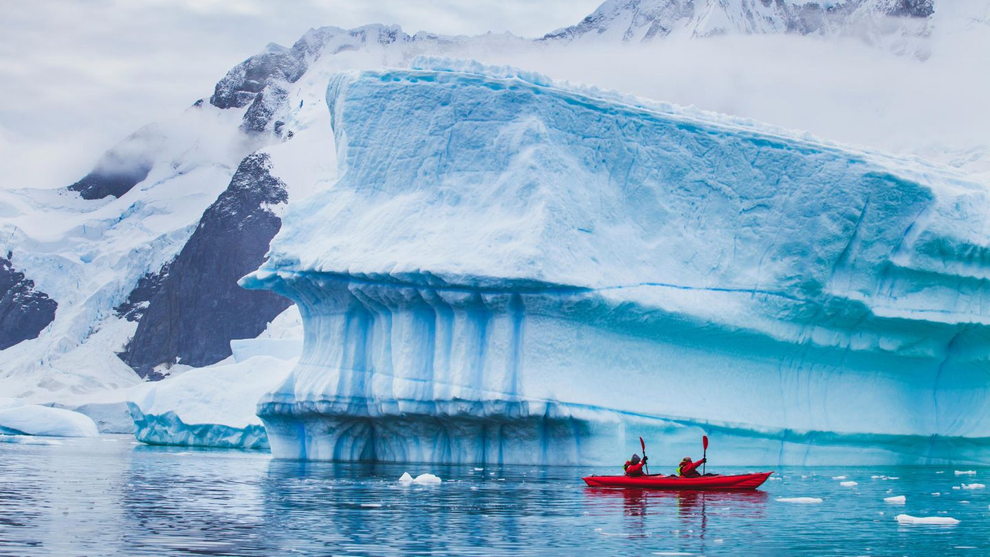 Menschen paddeln mit einem Kajak in der Nähe eines Eisbergs in der Antarktis Menschen paddeln mit einem Kajak in der Nähe eines Eisbergs in der Antarktis