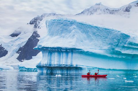 Menschen paddeln mit einem Kajak in der Nähe eines Eisbergs in der Antarktis