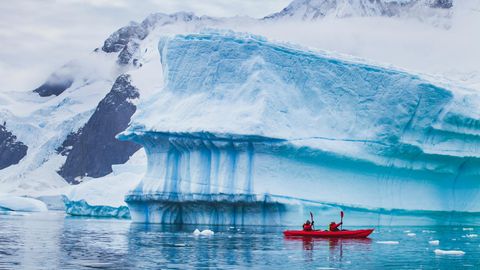 Menschen paddeln mit einem Kajak in der Nähe eines Eisbergs in der Antarktis